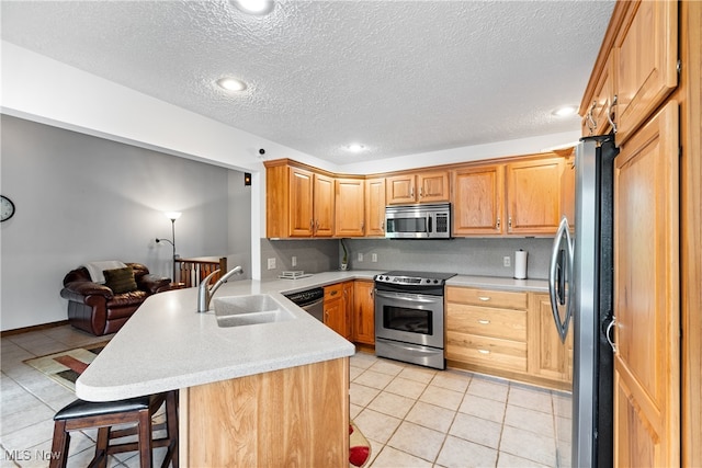 kitchen featuring a breakfast bar area, light tile patterned floors, kitchen peninsula, appliances with stainless steel finishes, and sink