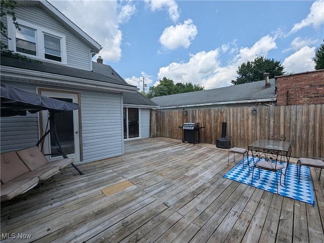 wooden terrace featuring outdoor dining area, a grill, and fence