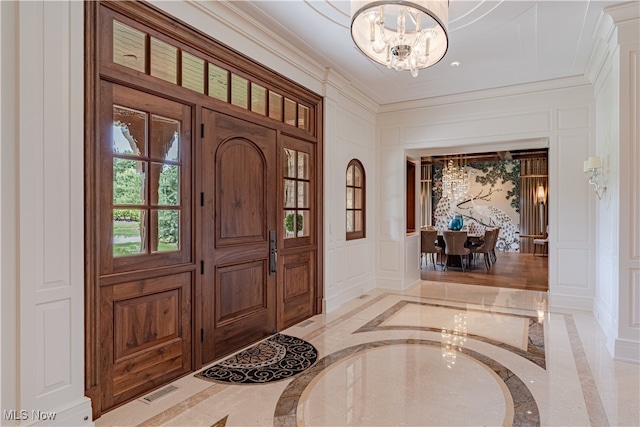 entrance foyer with crown molding, a notable chandelier, and ornate columns