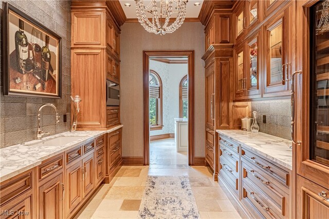 kitchen with sink, crown molding, decorative light fixtures, a chandelier, and light stone counters