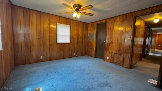 carpeted spare room featuring ceiling fan, wooden walls, and electric panel