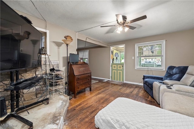 living room with a textured ceiling, ceiling fan, and dark wood-type flooring