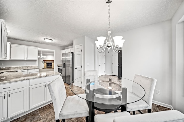 dining space featuring sink, a notable chandelier, a stone fireplace, and a textured ceiling