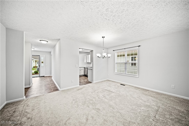 carpeted empty room with a chandelier and a textured ceiling