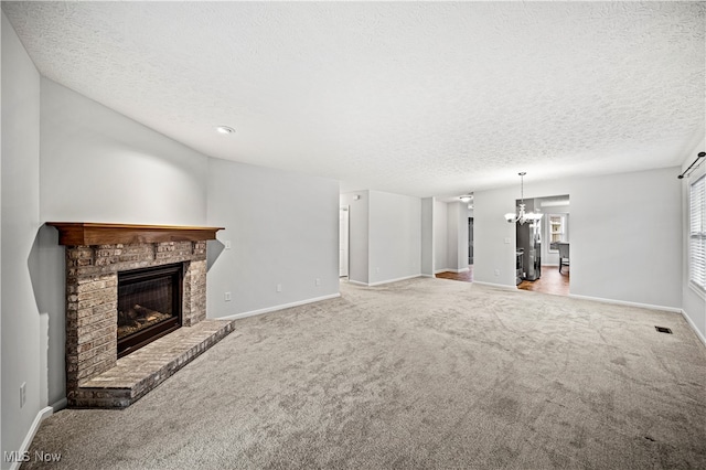 unfurnished living room with a fireplace, carpet, a textured ceiling, and a notable chandelier