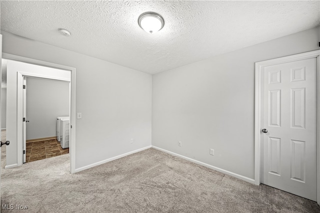 unfurnished room with light colored carpet, a textured ceiling, and washing machine and clothes dryer