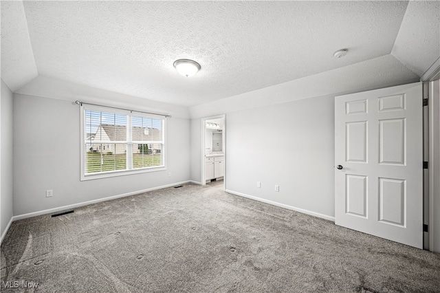 unfurnished bedroom with ensuite bathroom, carpet floors, and vaulted ceiling