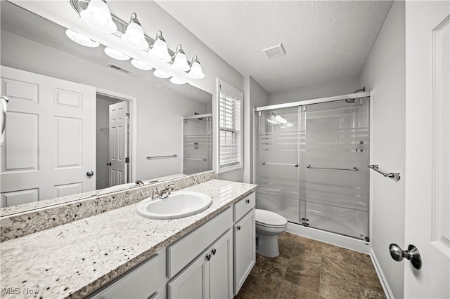 bathroom with vanity, toilet, a shower with door, and a textured ceiling