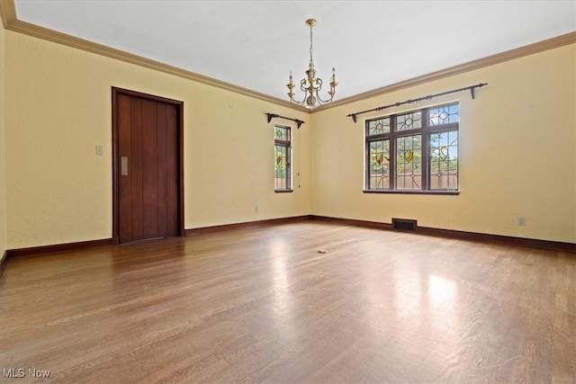 spare room featuring a chandelier, wood finished floors, visible vents, and baseboards