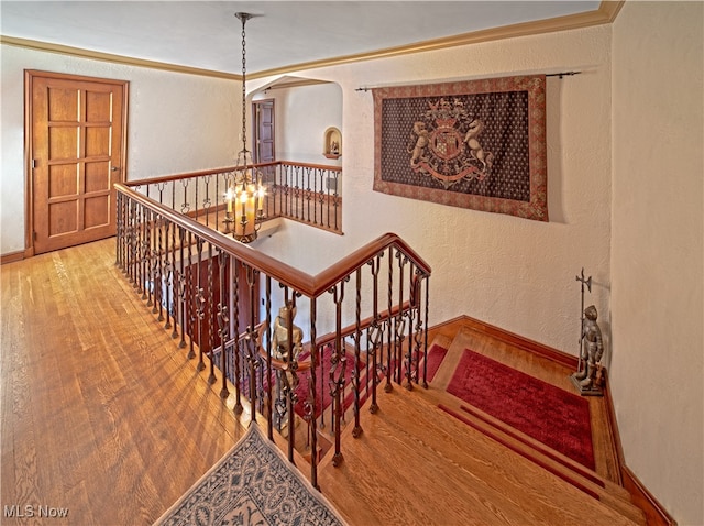 stairs with a textured wall, a notable chandelier, baseboards, wood-type flooring, and crown molding