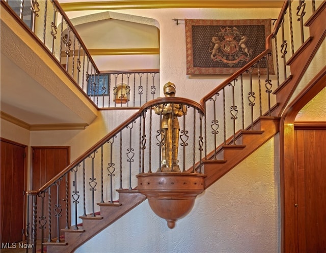 staircase with ornamental molding, a textured wall, and a high ceiling