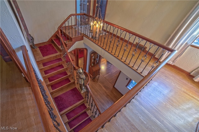 stairway with a notable chandelier, a textured wall, and wood finished floors