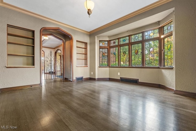 empty room with arched walkways, visible vents, baseboards, and wood finished floors