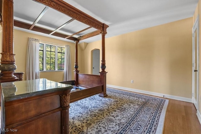 bedroom with baseboards, arched walkways, and wood finished floors