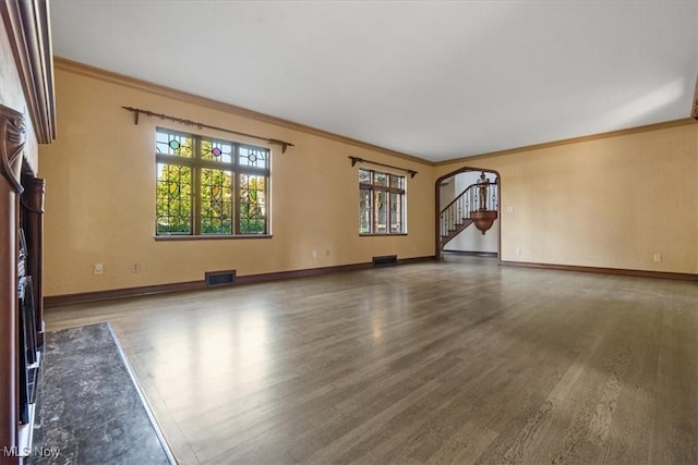 unfurnished living room with arched walkways, wood finished floors, visible vents, baseboards, and ornamental molding