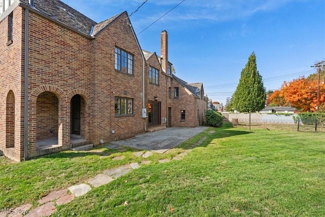 rear view of house featuring fence, a lawn, a patio, and brick siding