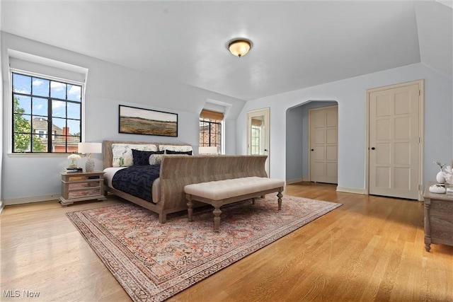 bedroom with arched walkways, light wood finished floors, and multiple windows