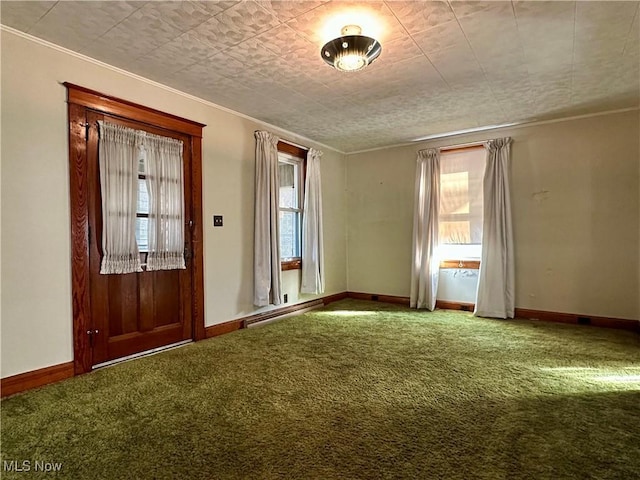 carpeted empty room featuring a baseboard heating unit, a healthy amount of sunlight, ornamental molding, and baseboards