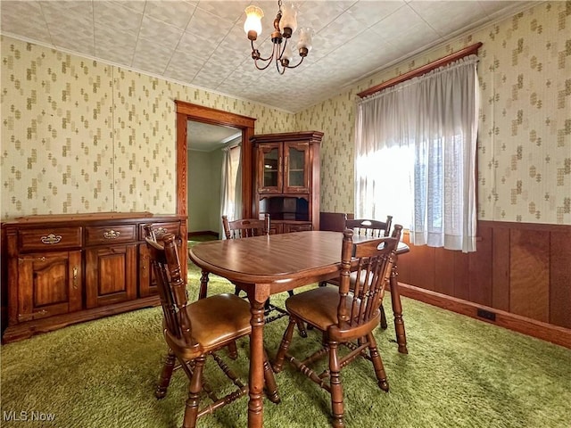 carpeted dining space with ornamental molding, wainscoting, an inviting chandelier, and wallpapered walls