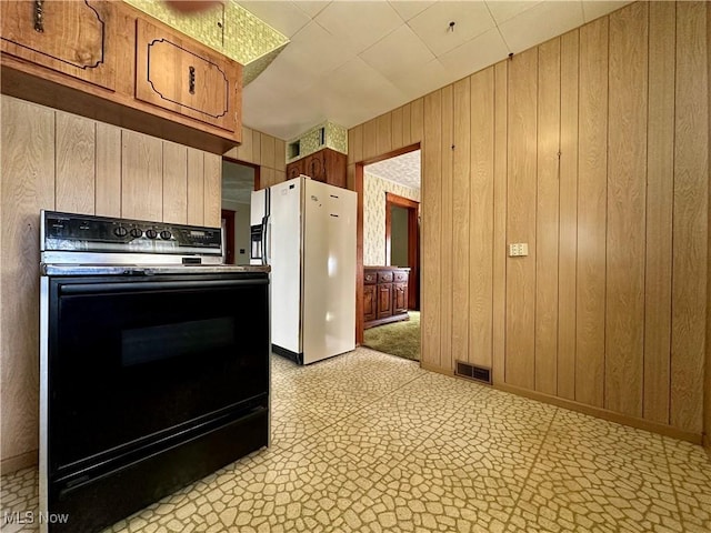 kitchen with visible vents, wood walls, stove, and freestanding refrigerator