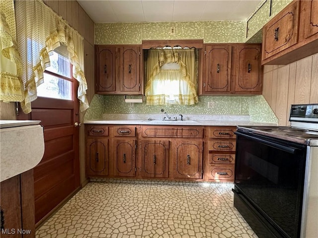 kitchen with light countertops, black electric range oven, decorative backsplash, brown cabinetry, and a sink