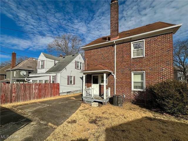 rear view of house featuring a chimney, fence, central AC, and brick siding