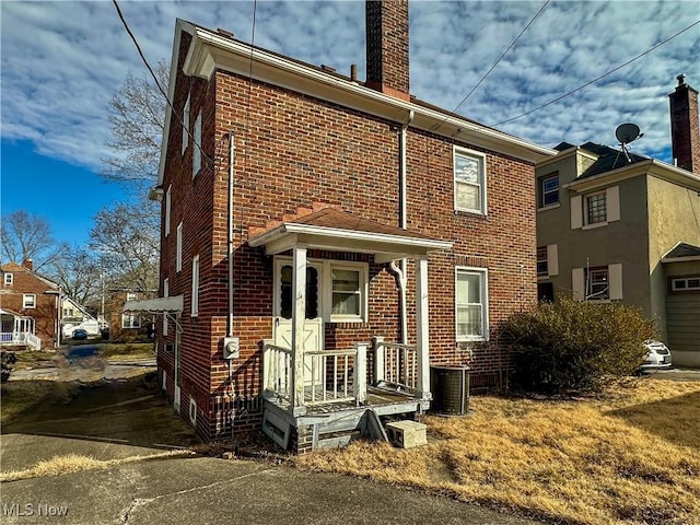 view of front of home with central air condition unit, a chimney, and brick siding