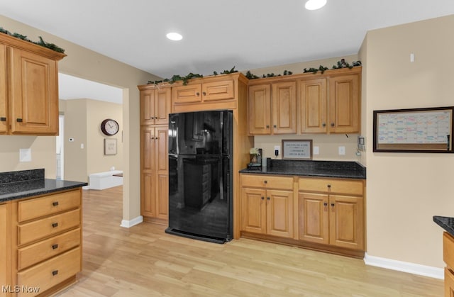 kitchen featuring dark stone countertops, light hardwood / wood-style flooring, and black fridge