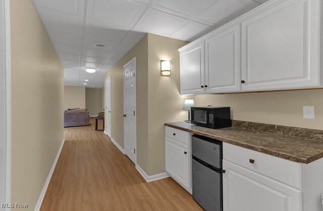 kitchen with a drop ceiling, white cabinetry, and light wood-type flooring