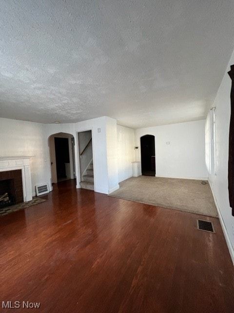 unfurnished living room featuring a textured ceiling, hardwood / wood-style floors, and a brick fireplace