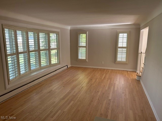 empty room with light hardwood / wood-style floors, a healthy amount of sunlight, and baseboard heating