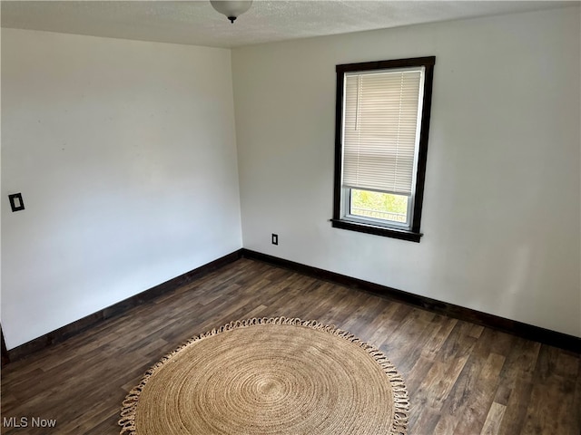 spare room featuring dark wood-type flooring and a textured ceiling