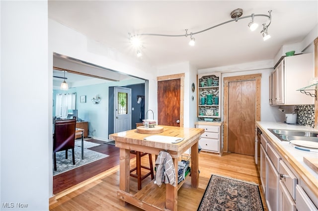 kitchen with white cabinets, pendant lighting, rail lighting, light wood-type flooring, and tasteful backsplash