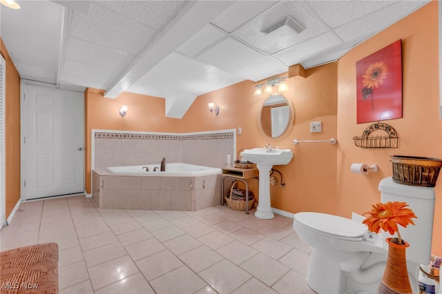 bathroom featuring a relaxing tiled tub, tile patterned flooring, toilet, and a paneled ceiling