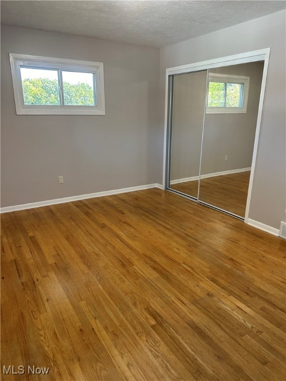 unfurnished bedroom with a textured ceiling, wood-type flooring, and a closet