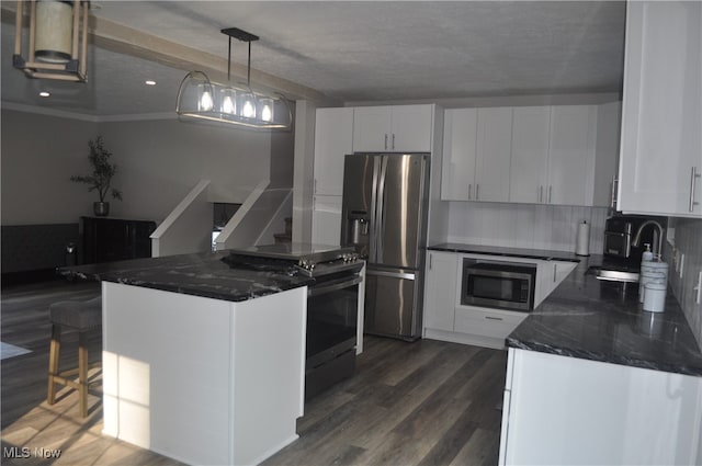 kitchen with appliances with stainless steel finishes, hanging light fixtures, dark wood-type flooring, white cabinets, and a breakfast bar area