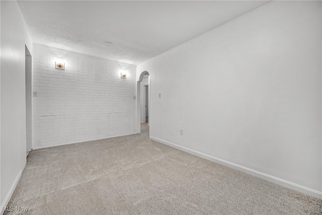 carpeted empty room featuring brick wall