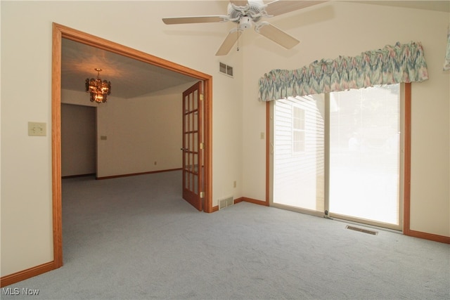 carpeted empty room featuring ceiling fan with notable chandelier, vaulted ceiling, and a wealth of natural light