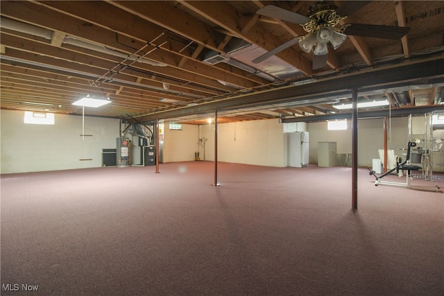 basement featuring white fridge, heating unit, ceiling fan, gas water heater, and carpet floors