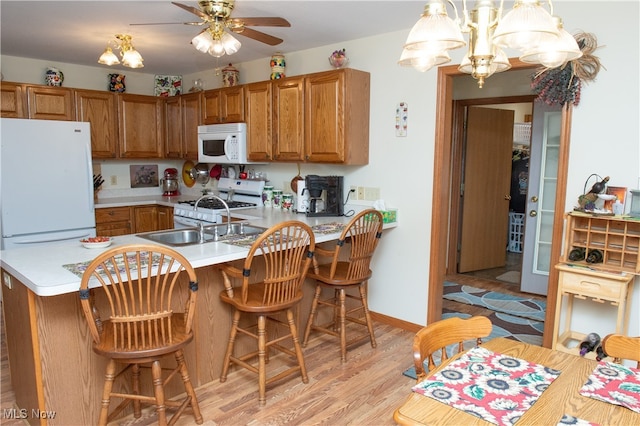 kitchen featuring kitchen peninsula, light wood-type flooring, a kitchen bar, and white appliances