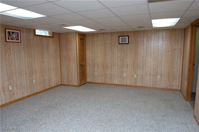 basement featuring a paneled ceiling, wooden walls, and light colored carpet