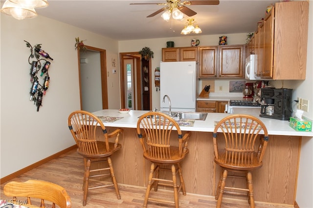 kitchen with ceiling fan, kitchen peninsula, a kitchen breakfast bar, light hardwood / wood-style floors, and white appliances