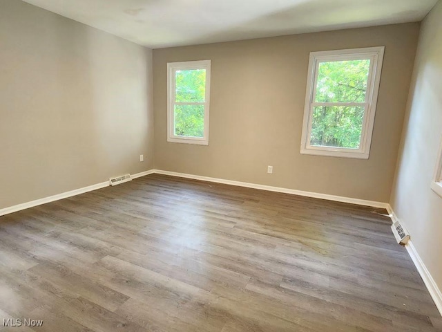 empty room with a wealth of natural light, wood finished floors, visible vents, and baseboards