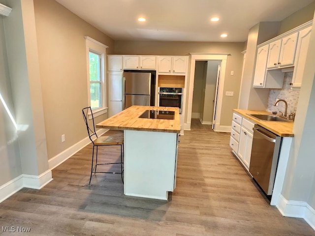 kitchen featuring stainless steel appliances, white cabinetry, sink, a kitchen island, and hardwood / wood-style floors