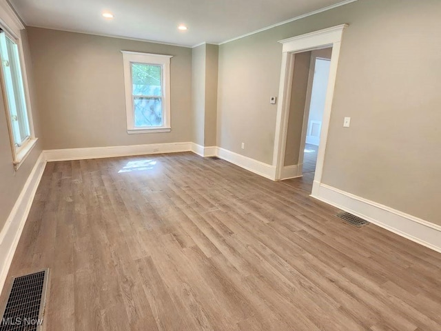 empty room with ornamental molding, light wood-style flooring, visible vents, and baseboards