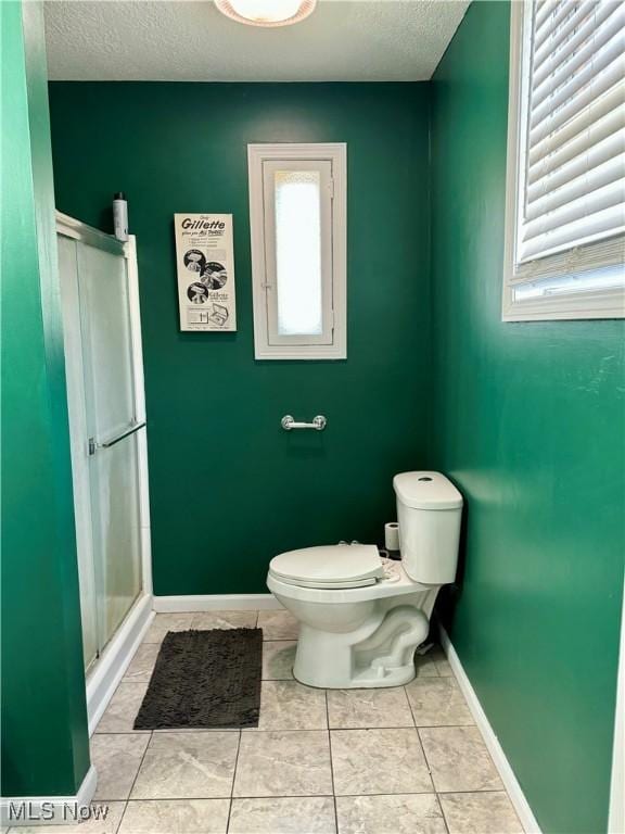 bathroom featuring plenty of natural light, toilet, a shower with shower door, and a textured ceiling