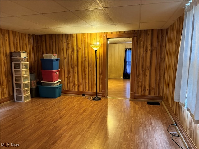 unfurnished room featuring wooden walls, a paneled ceiling, and wood-type flooring