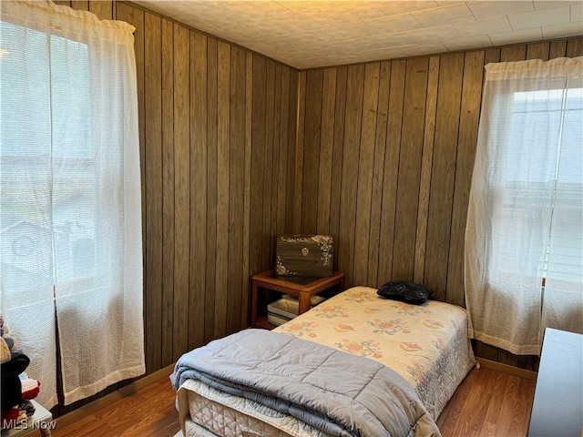 bedroom with wood walls, hardwood / wood-style flooring, and multiple windows