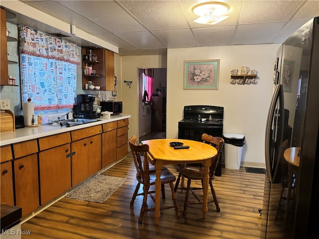 kitchen with decorative backsplash, light wood-type flooring, sink, a drop ceiling, and black appliances