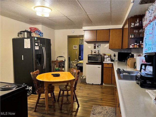 kitchen featuring stainless steel refrigerator with ice dispenser, dark hardwood / wood-style floors, a paneled ceiling, backsplash, and range